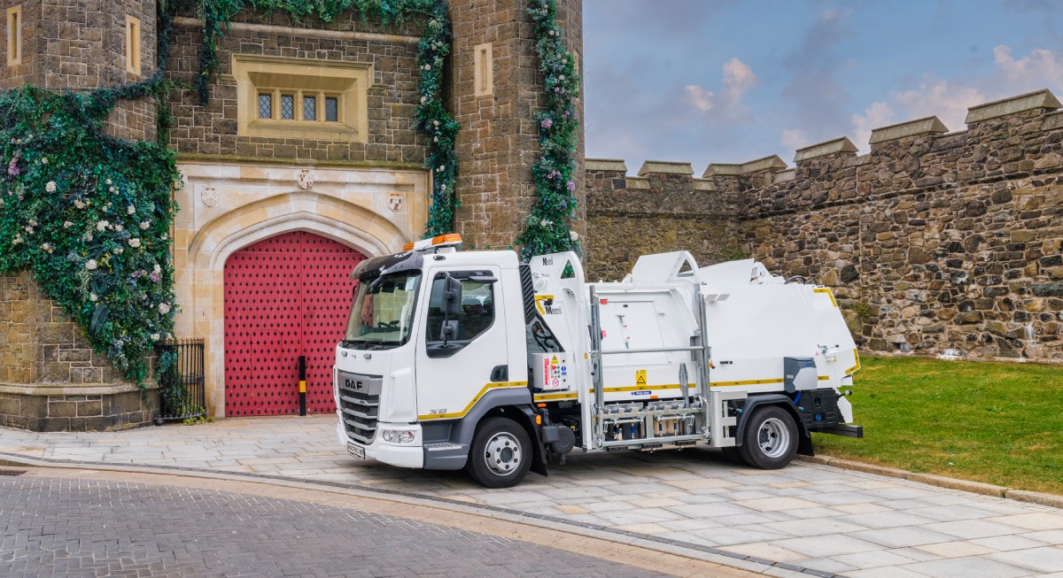 A garbage truck parked near a castle entrance with a large red door and stone walls decorated with plants.