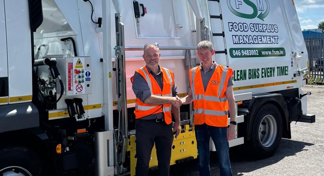 Two men in high-visibility vests shaking hands in front of a waste management truck.