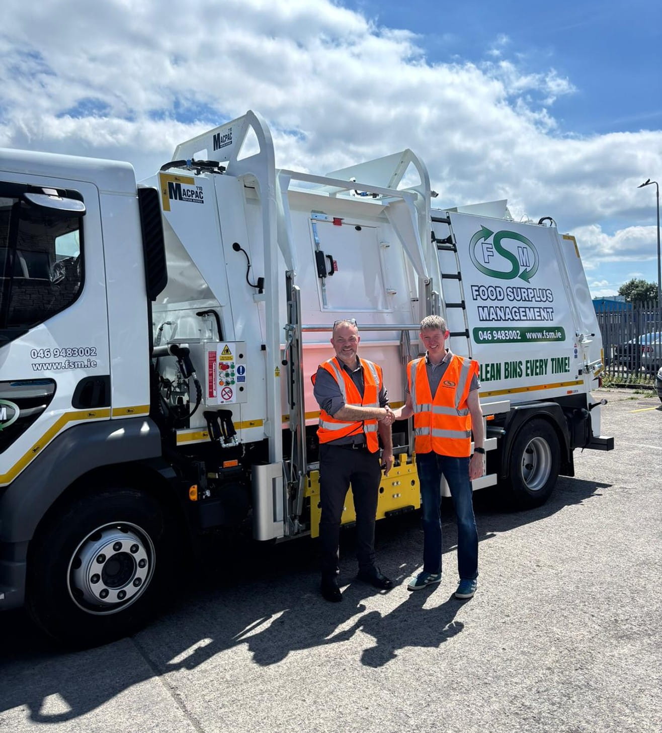 Two men in safety vests standing in front of a waste management truck.